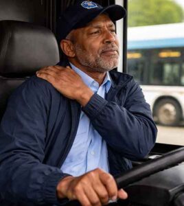 A public transit bud driver holds his shoulder due to back pain he is experiencing.